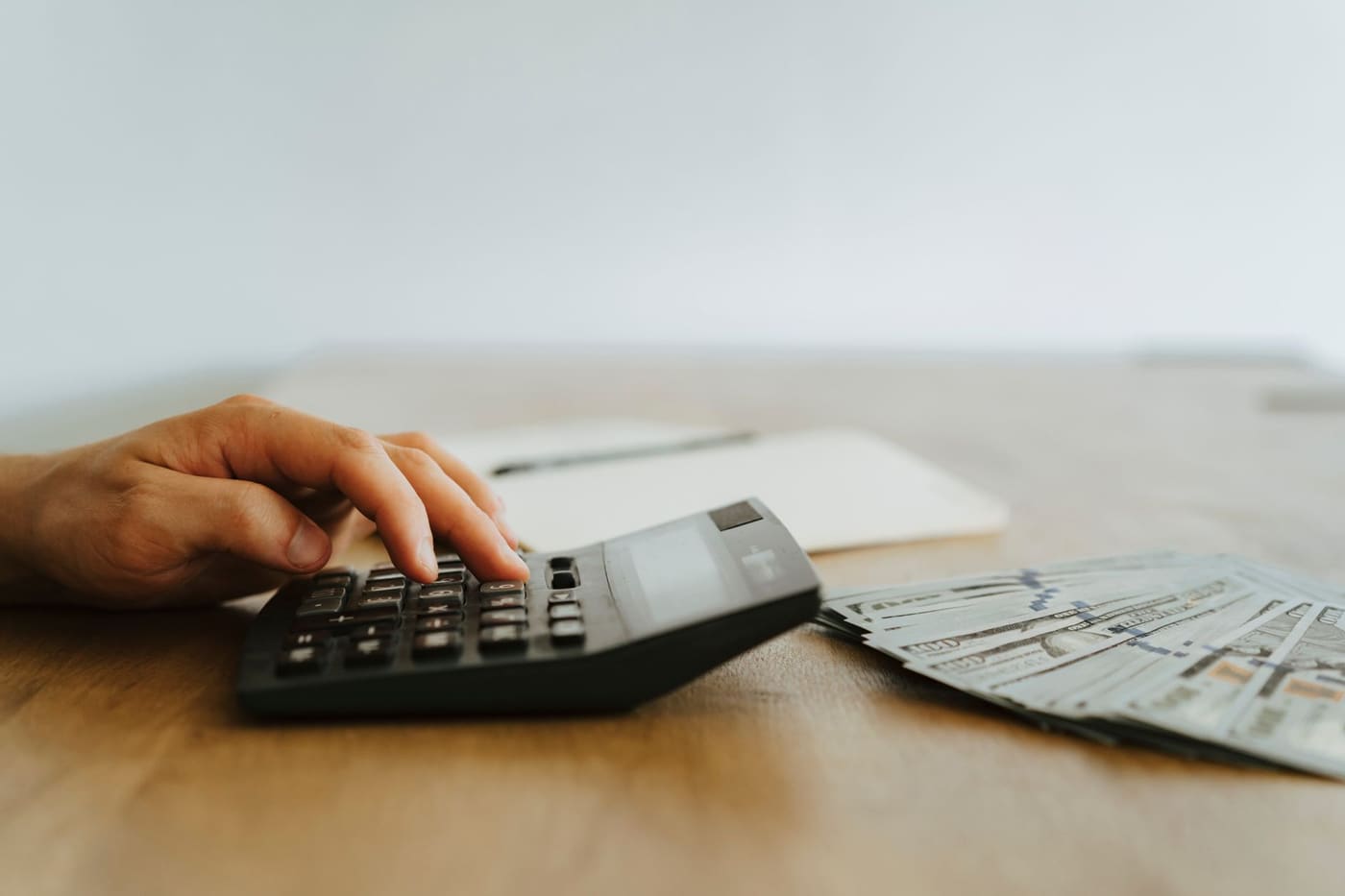 A hand using a calculator next to a fan of dollar bills