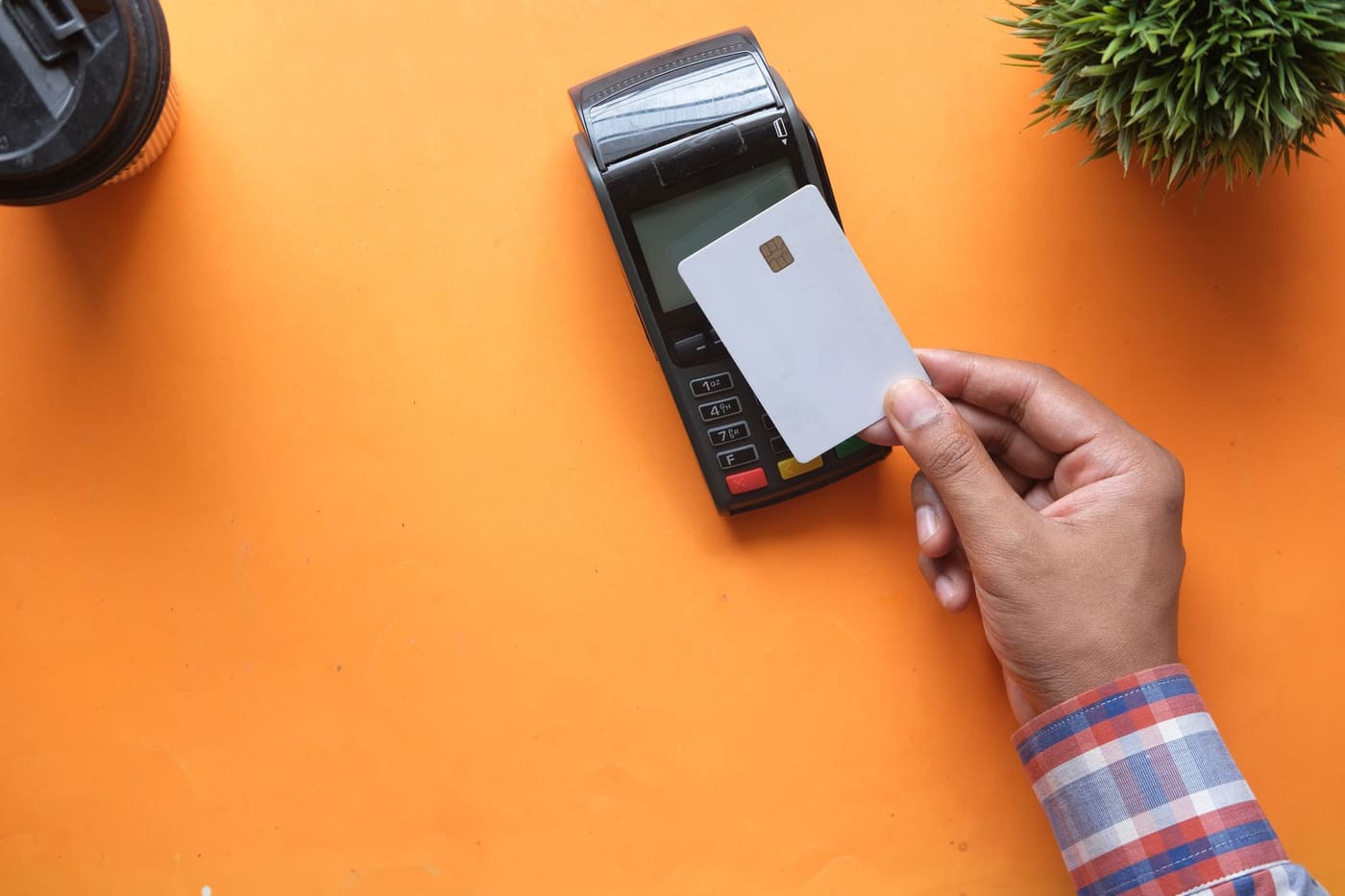 A person holding a card to a contactless payment reader on an orange table