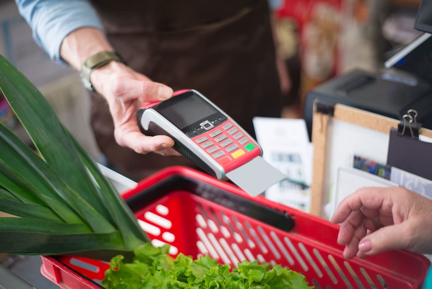 A hand holding a card reader over a basket of fresh produce at a grocery checkout
