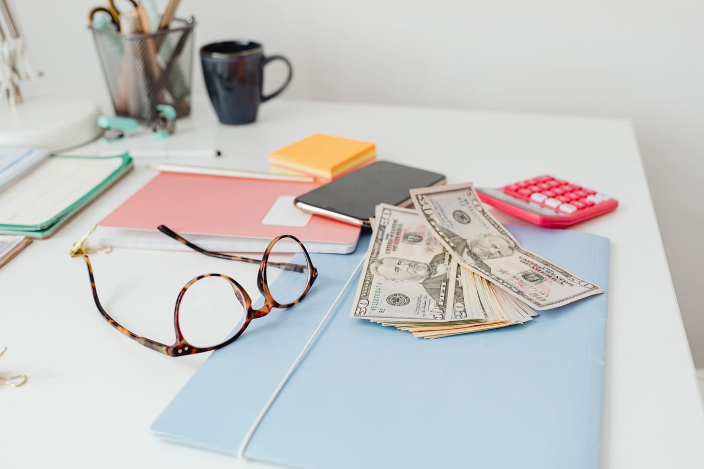 A desk with eyeglasses, dollar bills and stationery