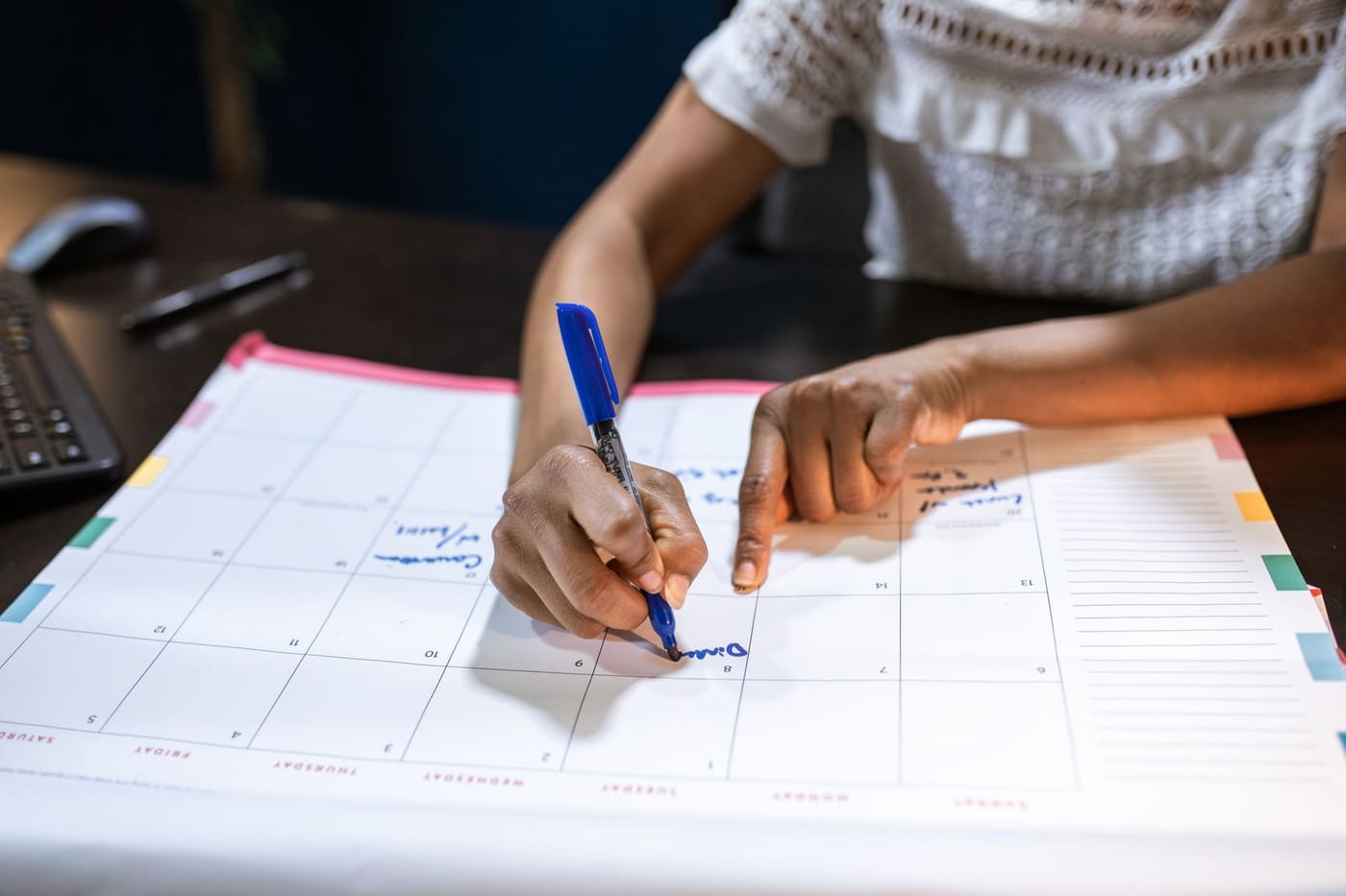 A hand marking dates on a desk calendar with a blue pen