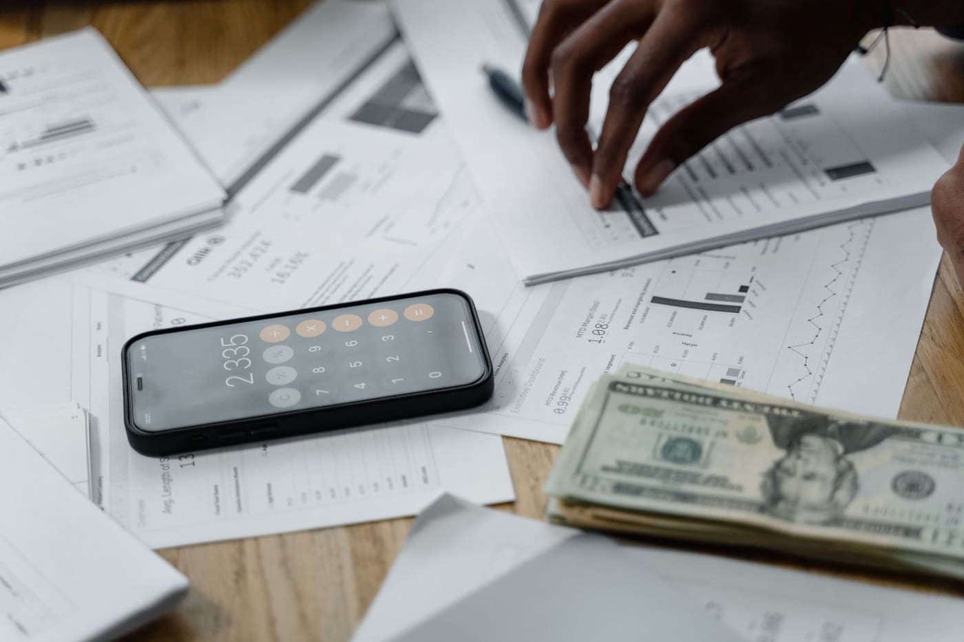 Hands working through figures with a smartphone, printed reports and cash on a table