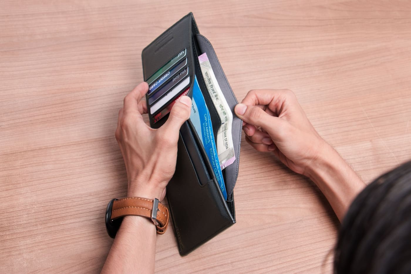 Hands sorting cards and cash in an open wallet on a wooden table